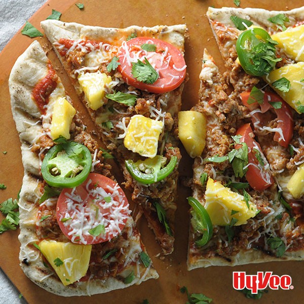 Thin grilled pizza crust topped with ground meat, jalapenos, pineapple chunks, sliced tomatoes, and shredded cheese