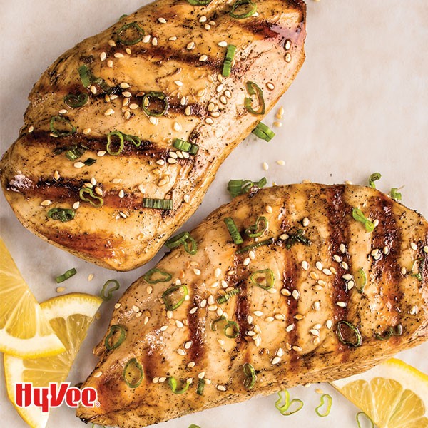 Grilled chicken breasts topped with sesame seeds, sliced green onions, and lemon wedges