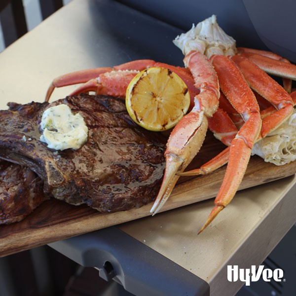 Grilled steak topped with compound butter, grilled crab legs and garnished with grilled halved lemon