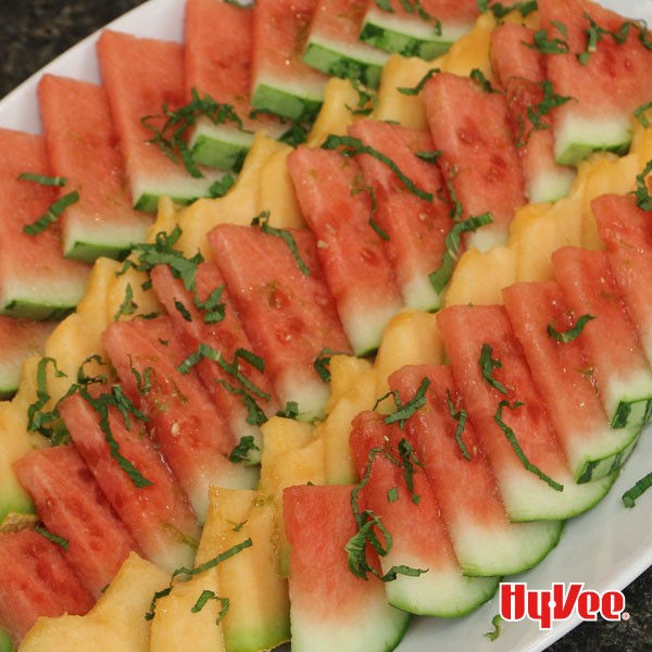 Watermelon and cantaloupe slices topped with thin slices of basil on a white serving platter