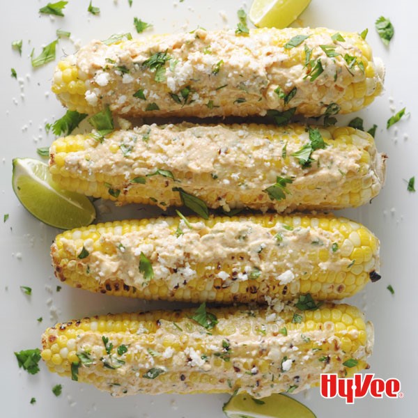 Grilled corn on the cob topped with crumbled cheese, cilantro, and garnished with lime wedges