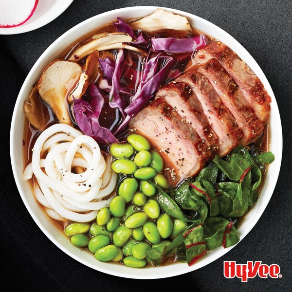 Bowl filled with noodles, edamame beans, red cabbage and sliced steak