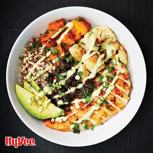 Bowl of seasoned chicen, sweet potatoes, cauliflower florets, quinoa, black beans and avocado slices, all drizzled in cilantro lime dressing and garnished with fresh cilantro