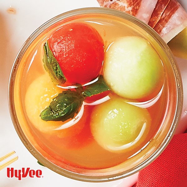 Glass filled with assorted melon balls and garnished with fresh basil leaves
