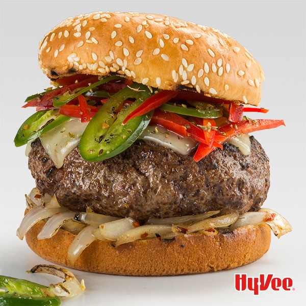 Bun topped with sliced onions, burger patty, white cheese, jalapenos, and bell peppers