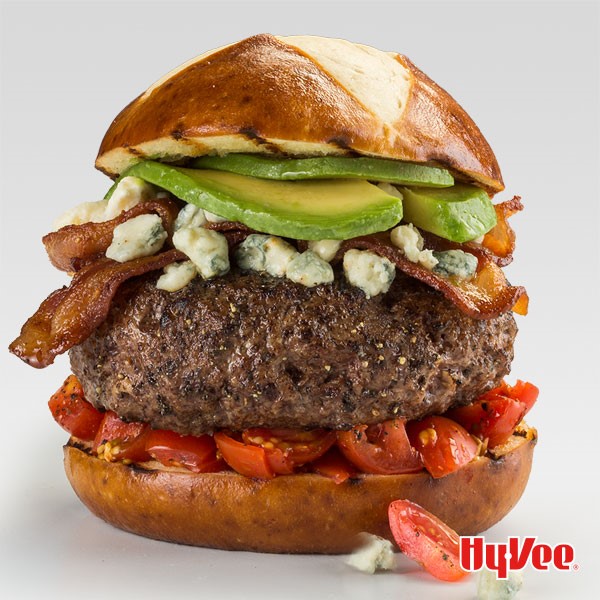 Grilled pretzel bun filled with cherry tomatoes, hamburger, blue cheese, bacon and avocado