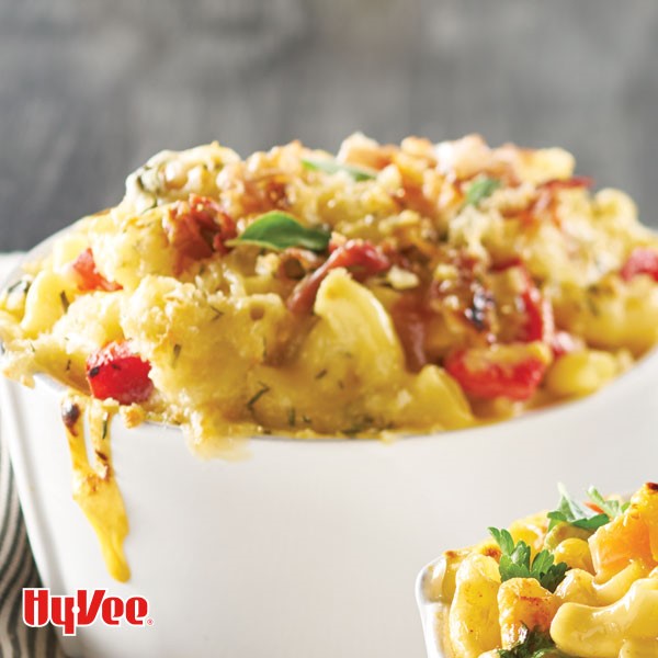White baking dish filled with mac and cheese and topped with crispy prosciutto, veggies, and basil leaves.