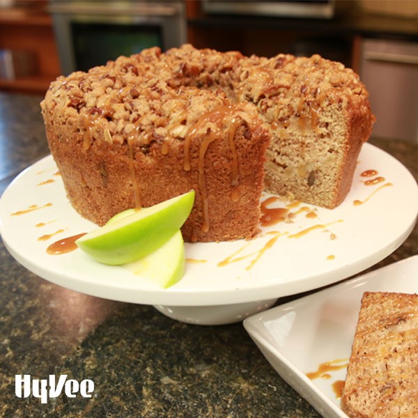 Apple pecan coffee cake drizzled in caramel on a white cake stand