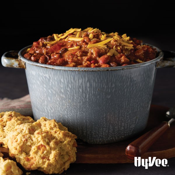Chili in a bowl with shredded yellow cheese and a side of biscuits