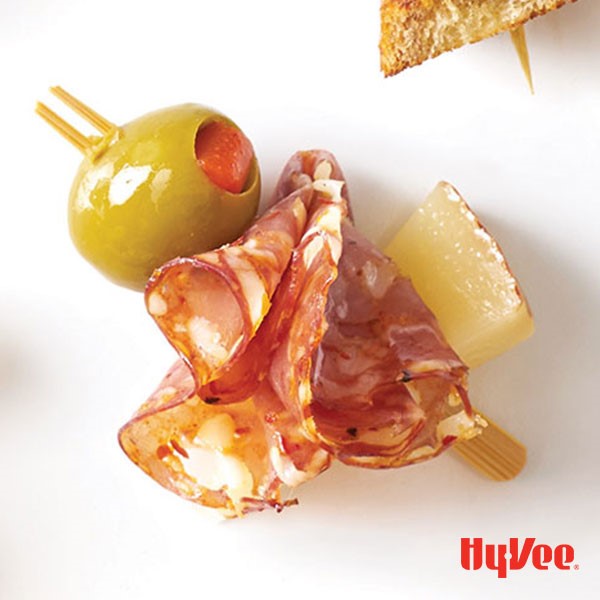 Small wooden skewer filled with salami, white cheddar, sharp cheddar and green olive