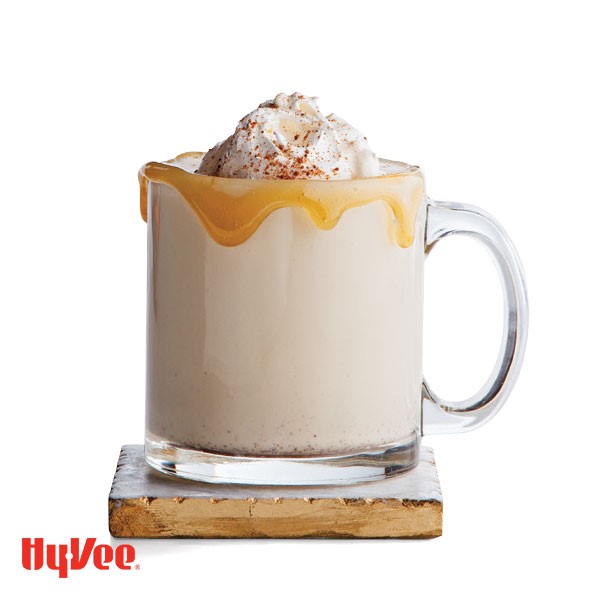 Caramel-rimmed glass of egg nog, garnished with whipped cream and a sprinkle of pumpkin pie spice