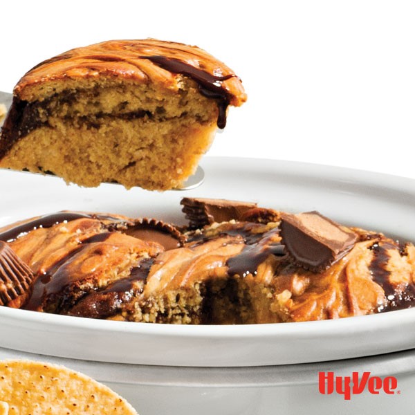 Peanut butter cake topped with chocolate syrup and Reese's mini peanut butter cups in a slow-cooker