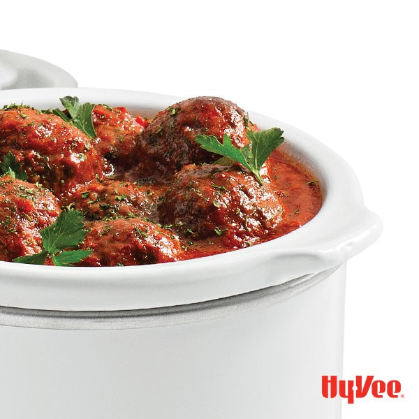 Slow cooker filled with meatballs and red sauce and garnished with fresh Italian parsley