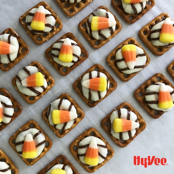 Waffle pretzels topped with Hershey's hugs and candy corn on parchment paper
