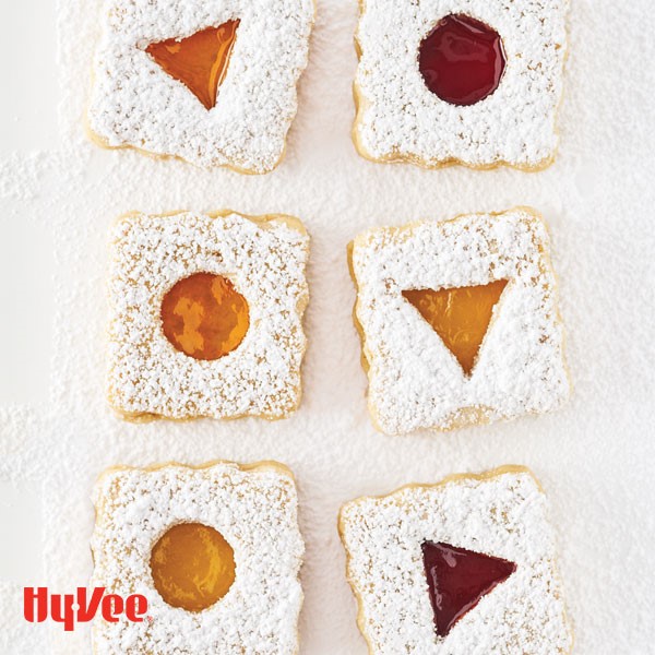 Almond cookies with fruit preserve filling coated in powdered sugar on parchment paper
