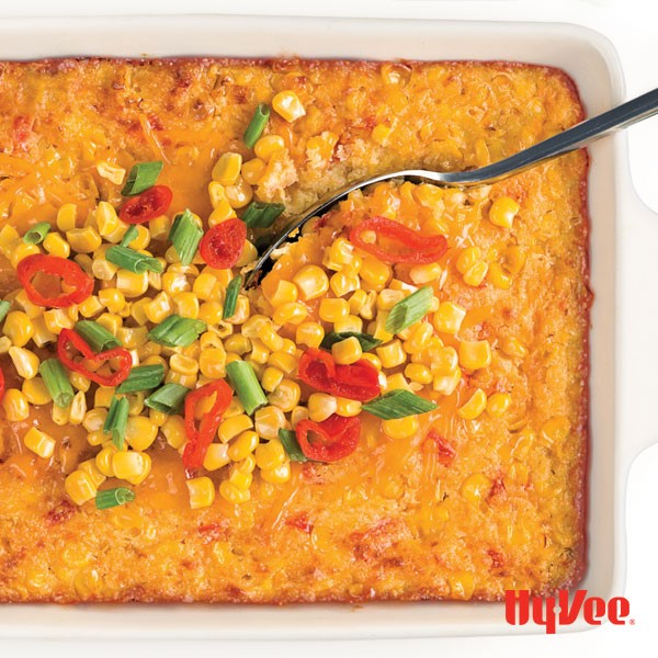 Casserole dish of cheesy corn casserole topped with corn, peppadew peppers and green onion 