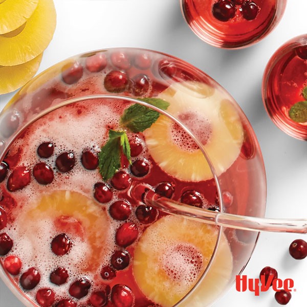 Container of sparkling punch with whole cranberries and sliced pineapples and garnished with fresh mint