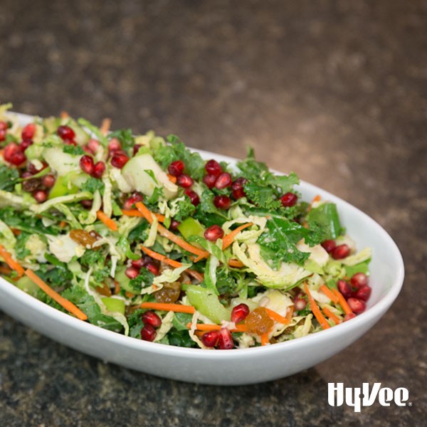 White serving dish topped with brussels sprouts, pomegranate seeds, and shredded carrots