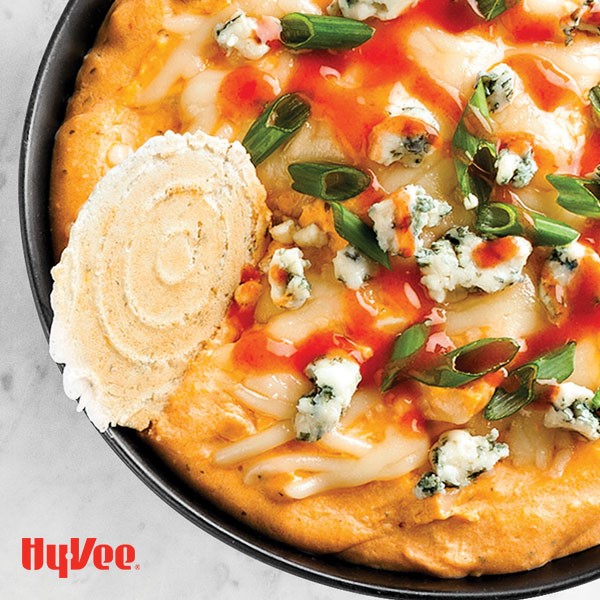 Bowl of buffalo dip garnished with green onions, cheese and a round cracker