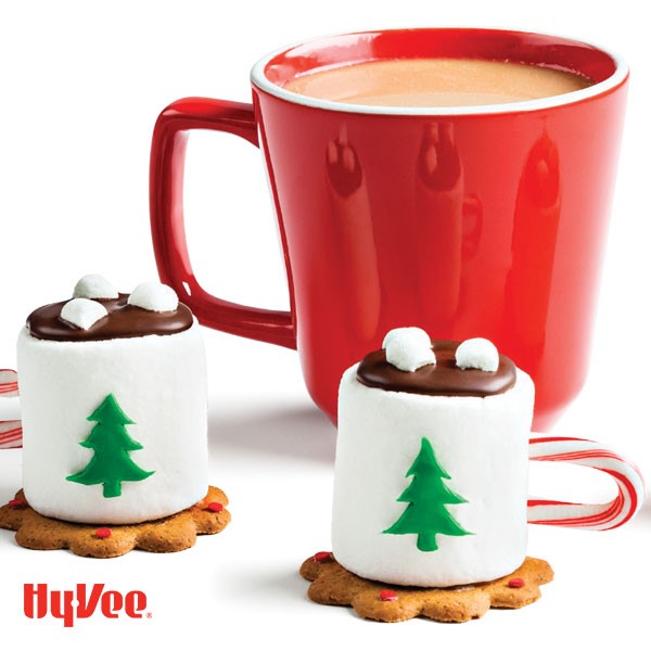 Large marshmallows on cookies with candy cane handles, green fondant Christmas tree cut out and red mug of cocoa on side