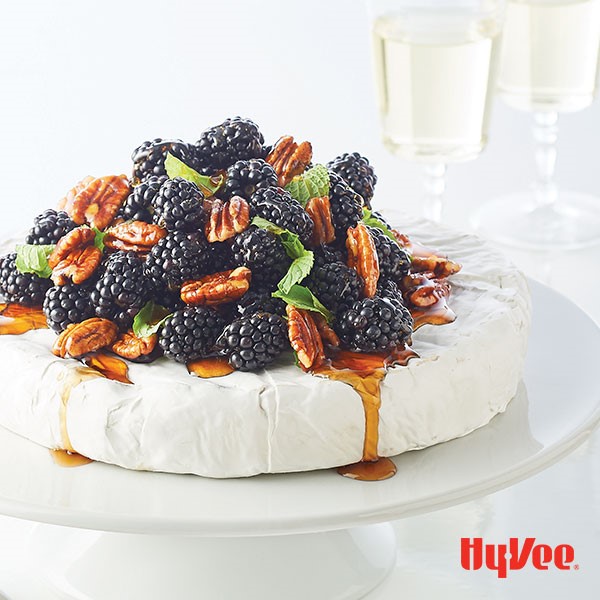 Brie cheese wheel topped with black berries, pecans, mint leaves, and syrup