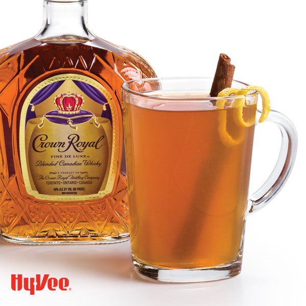 Mug filled with Hot Toddy , cinnamon stick, and lemon peel with Crown Royal bottle in background