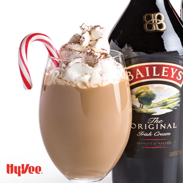 Wine glass filled with coffee, whipped cream, and candy cane next to a bottle of Irish Cream