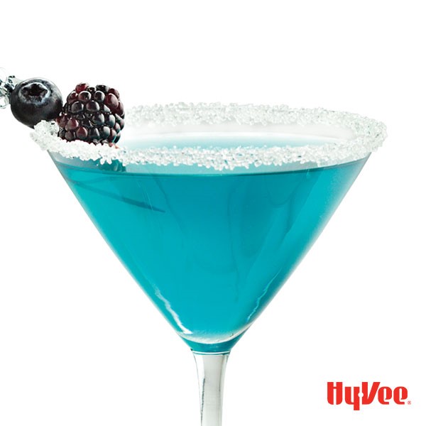 Sugar-rimmed martini glass filled with blue martini and garnished with fresh berries