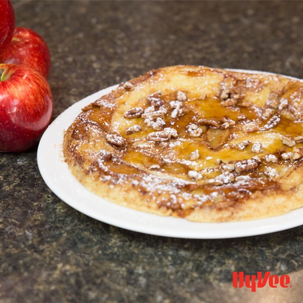 White plate topped with pancake drizzled with syrup, chopped pecans, and powdered sugar