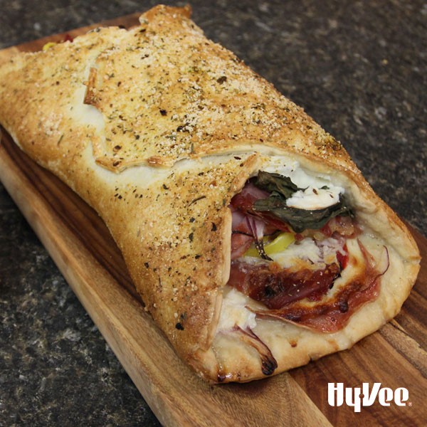 Stromboli wrapped around cheese, sliced meat, and onions on a wooden cutting board