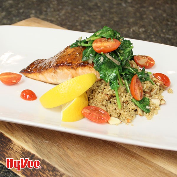 Plate of salmon topped with spinach and tomatoes over a bed of quinoa and garnished with lemon wedges