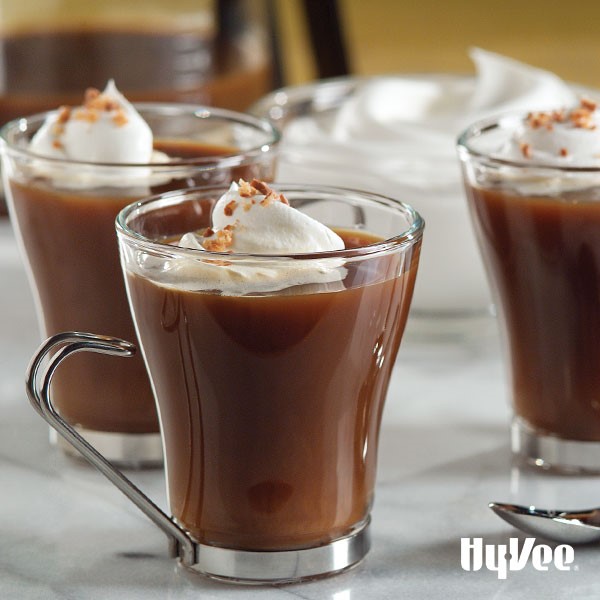 Glass mug of caramel coffee topped with whipped topping and chopped chocolate-covered toffee bar