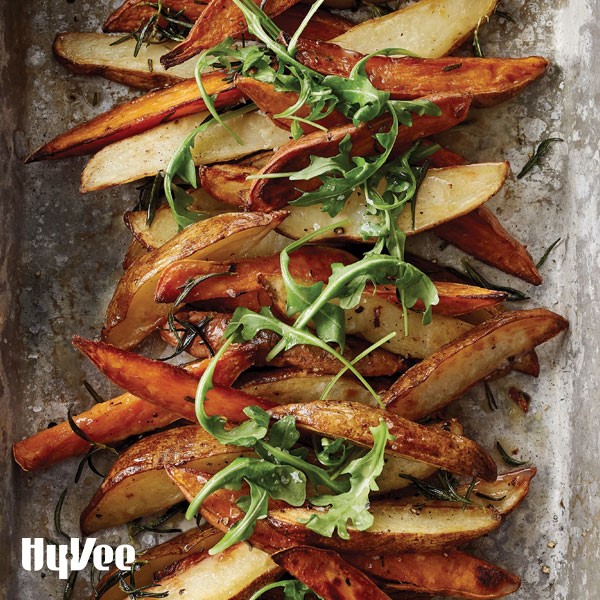 Roasted potato wedges on metal sheet pan topped with fresh rosemary and fresh arugula