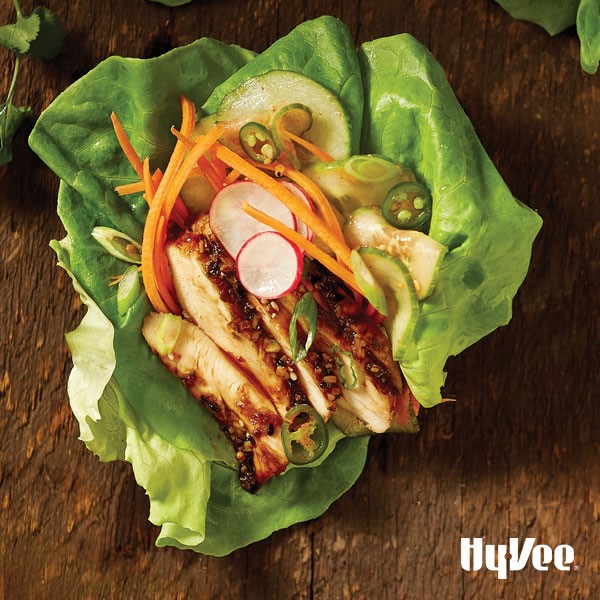 Lettuce leaves topped with sliced chicken  chicken, shredded carrots, sliced radishes, and sliced cucumbers