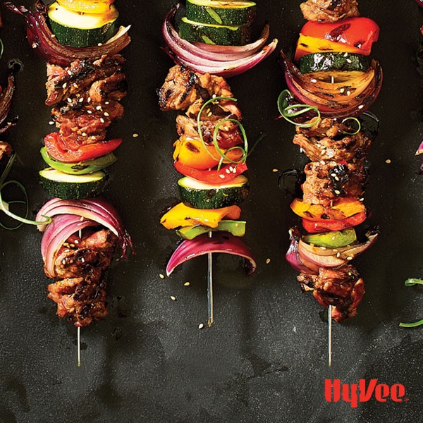 Skewers of beef, red onion, multi colored peppers, and zucchini on metal skewers sprinkled with sesame seeds