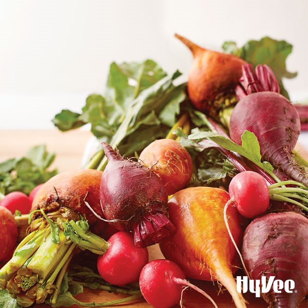Raw red and yellow beets with raw radishes with tops on a wooden cutting board