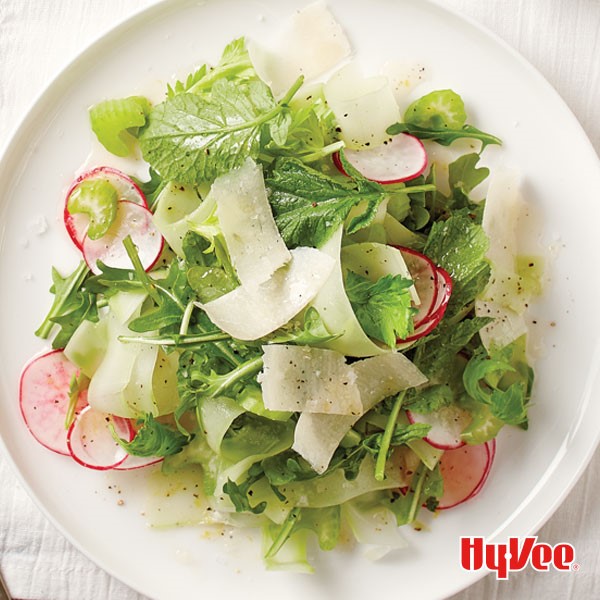 White plate topped with mixed greens, thinly sliced radishes, and shaved Parmesan cheese