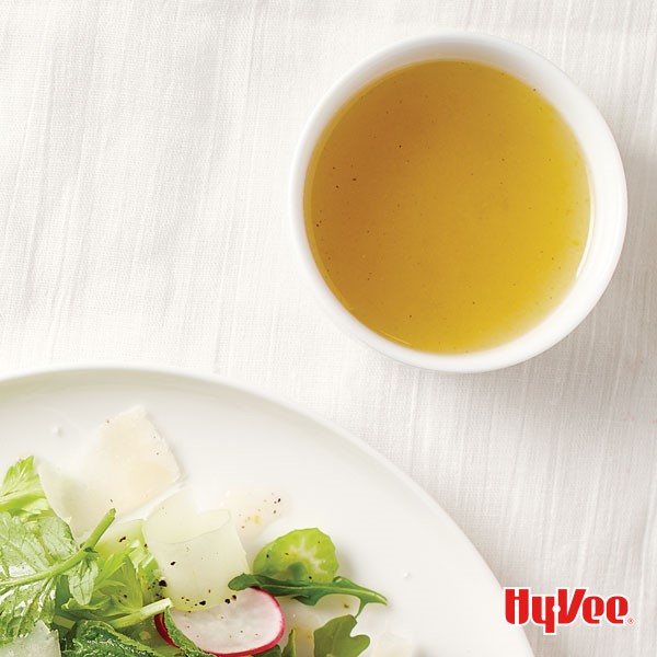 Lemon-honey vinaigrette in a small bowl next to a leafy green salad