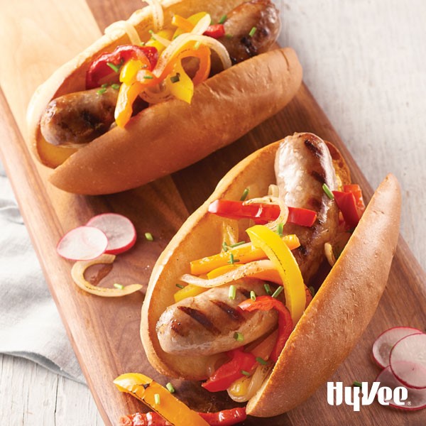 Grilled brats in bun with onions, peppers on a bun
