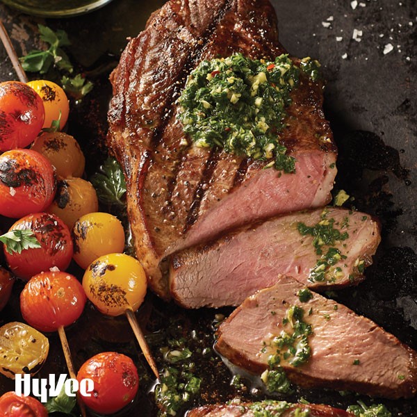 Sliced steak with green chimichurri sauce next to skewered and grilled yellow and red tomatoes