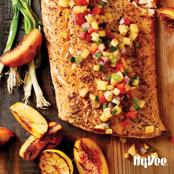 Salmon topped with peach salsa on a wooden plank