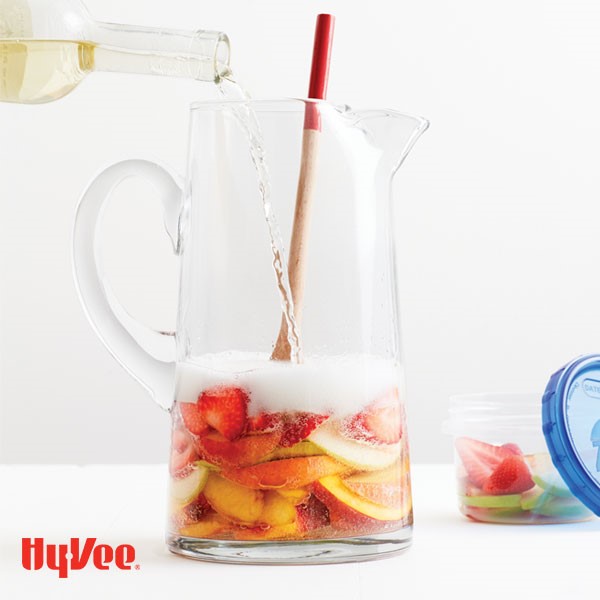 Pitcher with sliced fruit and sparkling wine poured into a glass pitcher
