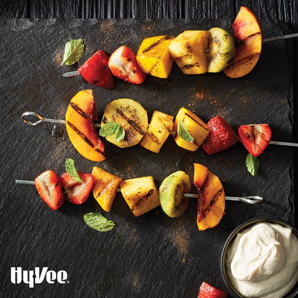 Grilled strawberries, peaches, pineapple, and kiwi on metal skewers and garnished with fresh mint leaves