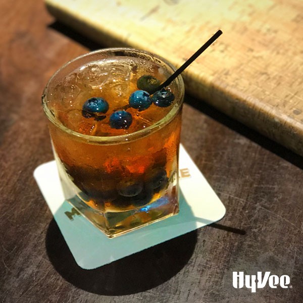 Drink in a glass topped with ice, whole blueberries, and black straw