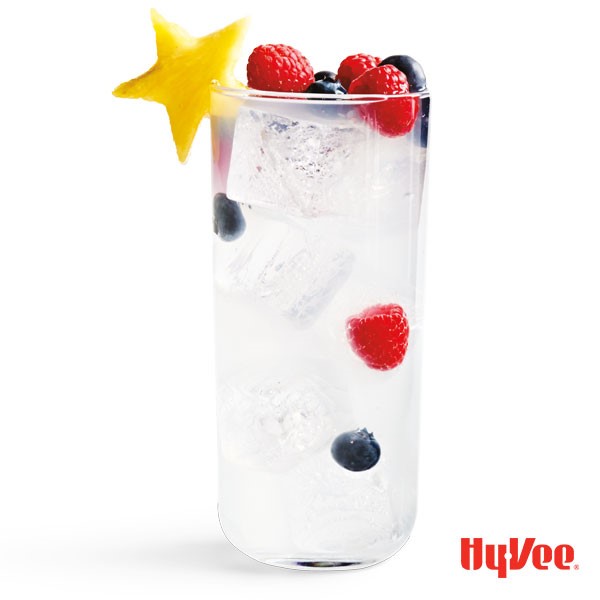 Tall glass of coconut vodka refresher garnished with star-shaped pineapple, blueberries and raspberries
