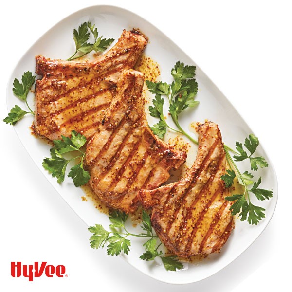 Bone-in pork chops topped with mustard sauce and garnished with Italian parsley