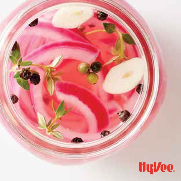 Sliced red onions with pepper corns, sliced garlic, and fresh thyme in a mason jar