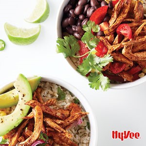 Bowls fileld with shredded chicken, rice, tomatoes, black beans, sliced avocados, cilantro, and sliced limes on the side