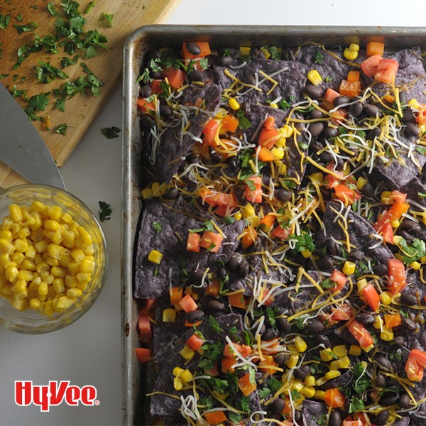 Blue tortilla chips topped with yellow corn, shredded cheese, chopped cilantro, black beans and chopped tomatoes