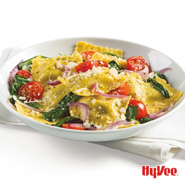 Ravioli with Parmesan cheese, sliced red onions, cherry tomatoes, and spinach inside a white bowl